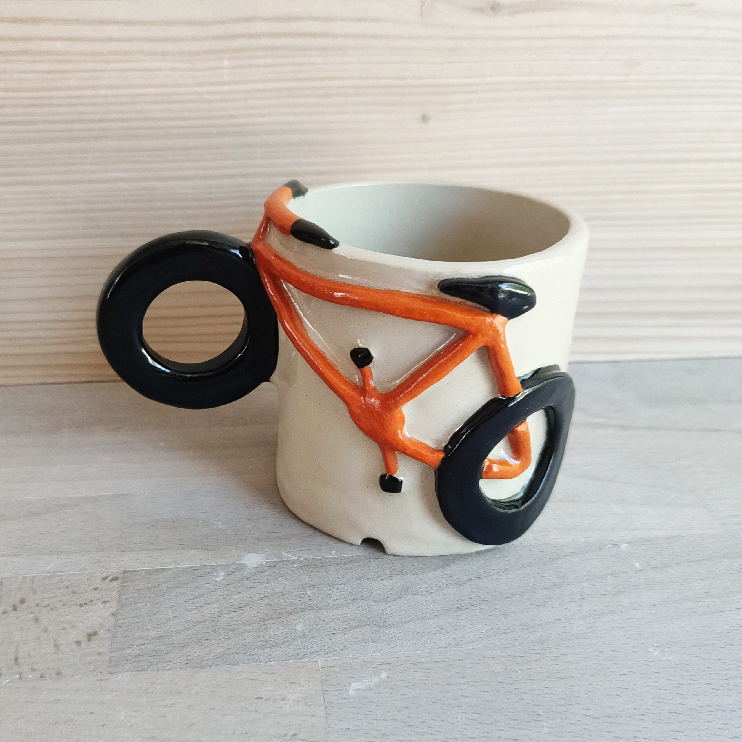 Photographie d'une tasse avec un vélo orange dessus. Le vélo est en volume et l'une des roue est l'anse de la tasse